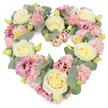 A softly coloured, heart-shaped wreath takes centre stage against a clean white background, its gentle hues and generous fullness creating an atmosphere of peace and affection. The heart is flawlessly formed, its curves smoothed by a dense covering of blooms that sit closely together without gaps, giving a sense of completeness and attentive design. Creamy ivory and pale yellow roses act as the primary feature, their velvety petals spiralling towards a rounded, open form that feels both classic and comforting. Between these roses, numerous pastel pink carnations are clustered in small groups, their frilled edges and layered petals lending a romantic, cushiony texture. Nestled among them, lisianthus blossoms in richer pink and soft mauve tones reveal slightly more open, trumpet-shaped petals, adding variety in form and gentle depths of colour. Throughout the wreath, stems of silvery-green eucalyptus weave naturally, the rounded leaves providing a cool contrast and creating a framing effect that emphasises the heart outline. Tiny yellow-green buds appear here and there, subtle details that suggest fresh, just-opened flowers and meticulous, recent preparation. The mood of the piece is reflective and full of love, something you could imagine being delivered quietly to a service in Somers Town or a nearby venue along Euston Road, perhaps chosen by a family remembering someone dear. With its calm palette of pink, cream, and green, the wreath expresses sympathy and remembrance without feeling heavy, making it suitable for funerals, memorials, and anniversary tributes. Against the uncluttered white background, every nuance of petal, leaf, and colour becomes part of a serene, heartfelt message of farewell.